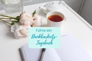 Bild mit Blumen, Tee und einem Journal und dem Schriftzug Führe ein Dankbarkeits-Tagebuch von Christa Daschner