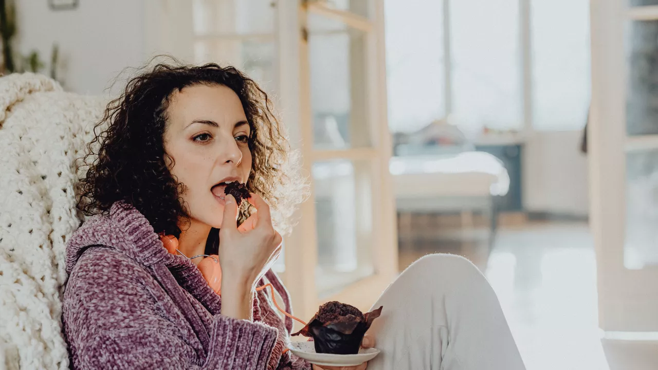 Frau sitzt entspannt und isst Schokomuffin - Heißhunger verstehen emotionales Essen