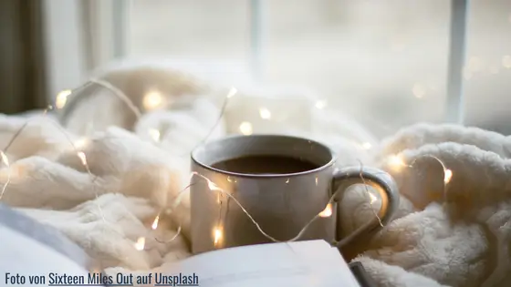 Kaffeetasse vor gemütlicher Decke und lichtern mit Buch - Essen zur Beruhigung - Veränderung beginnt mit Verständnis